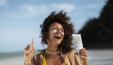Vrolijke afro-amerikaanse vrouw op het strand met zonnebrandcreme op haar wangen en in haar hand