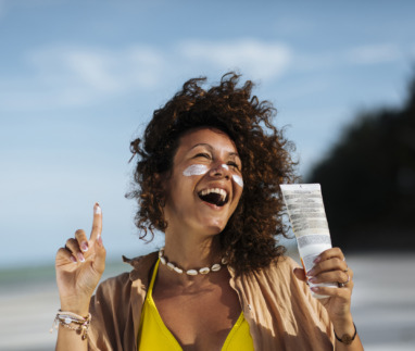 Vrolijke afro-amerikaanse vrouw op het strand met zonnebrandcreme op haar wangen en in haar hand