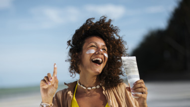 Vrolijke afro-amerikaanse vrouw op het strand met zonnebrandcreme op haar wangen en in haar hand