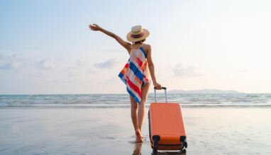 Vrouwelijke soloreiziger met koffer op strand