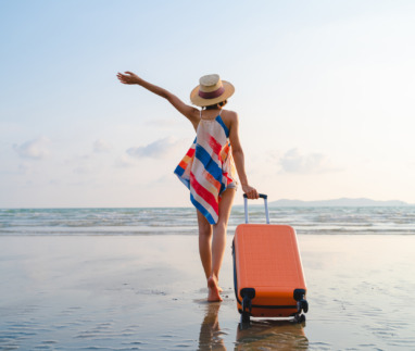 Vrouwelijke soloreiziger met koffer op strand