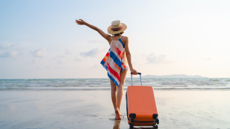 Vrouwelijke soloreiziger met koffer op strand
