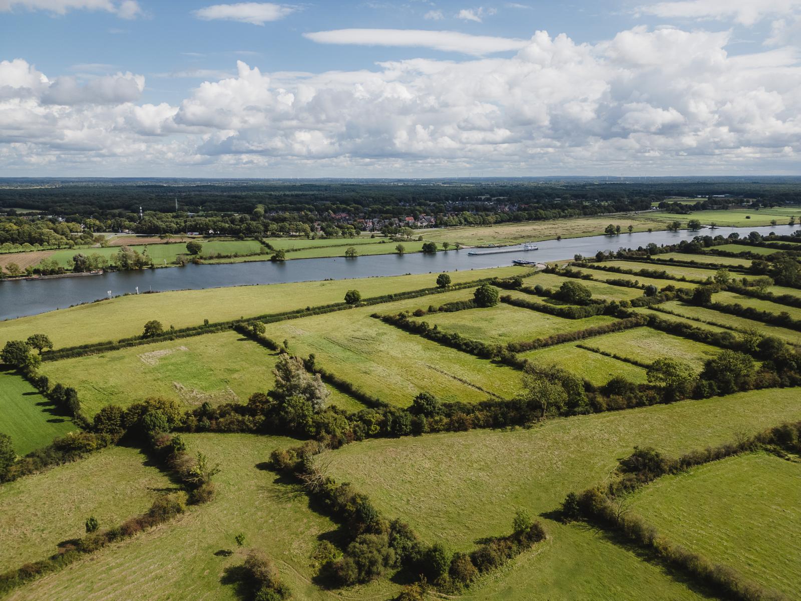 Luchtfoto van de Maasheggen met een mozaïek van groene weilanden en vlecht綿eggen langs de rivier de Maas.