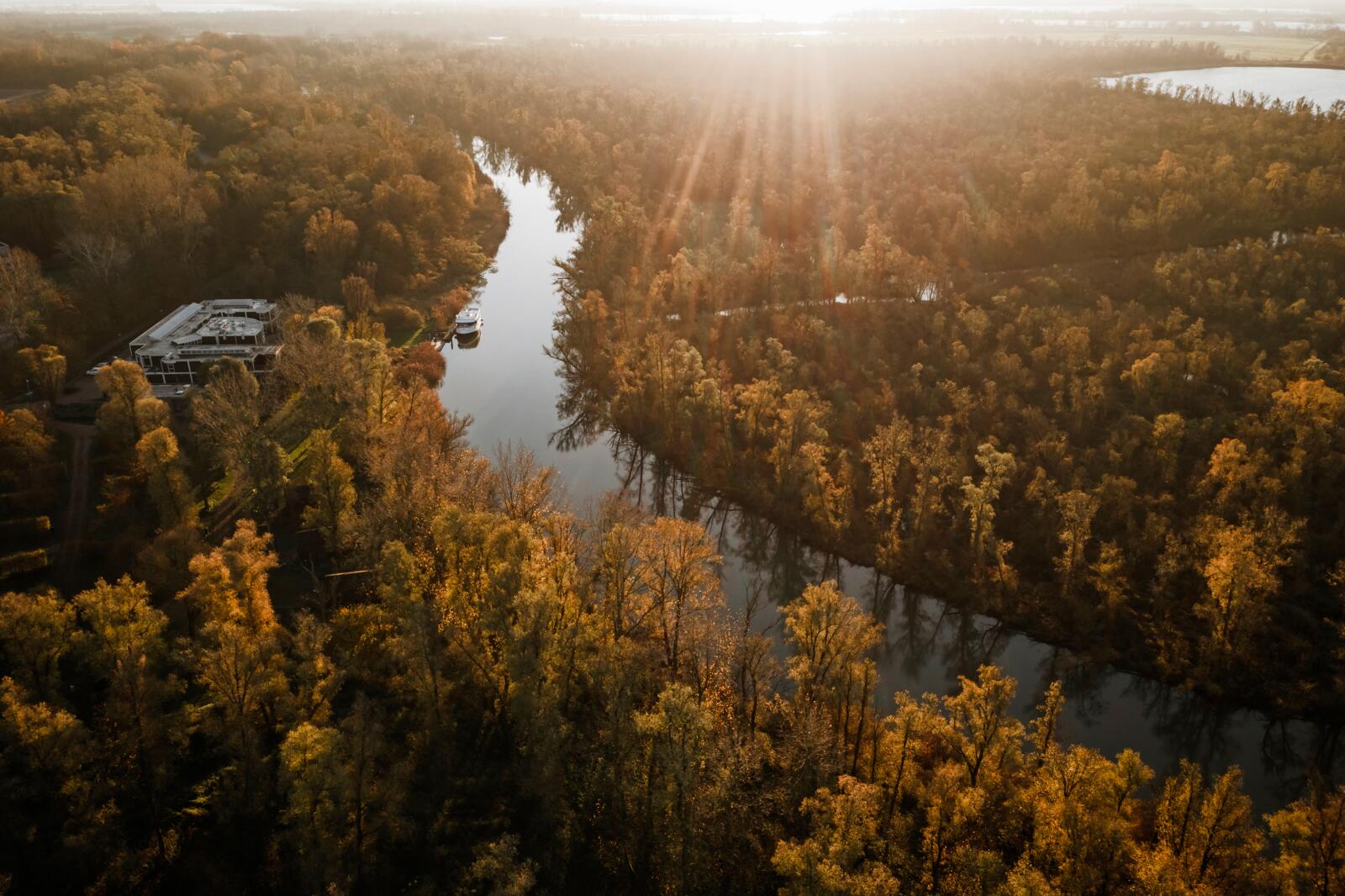 Luchtfoto van Stayokay Dordrecht aan een kronkelende rivier in een goudkleurig bos tijdens zonsopgang