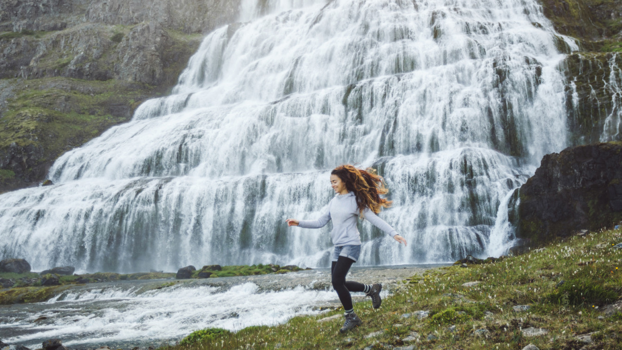 Vrouw rent vrolijk langs waterval in IJsland