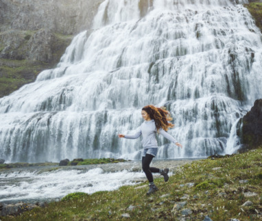 Vrouw rent vrolijk langs waterval in IJsland