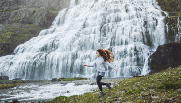 Vrouw rent vrolijk langs waterval in IJsland