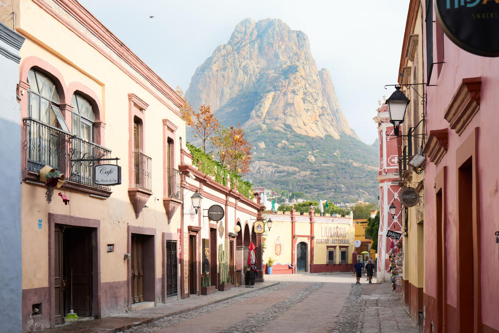 Een charmant straatbeeld in het dorp Bernal, Mexico, met kleurrijke koloniale gebouwen aan weerszijden en de indrukwekkende Peña de Bernal monoliet op de achtergrond.