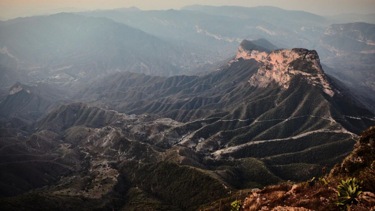 Een weids berglandschap bij zonsopgang gezien vanaf het uitkijkpunt Mirador Cuatro Palos in Mexico, met diepe valleien en een opvallende rotsformatie onder een zachte ochtendlucht.