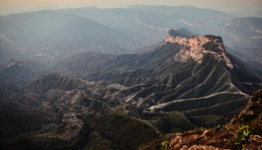 Een weids berglandschap bij zonsopgang gezien vanaf het uitkijkpunt Mirador Cuatro Palos in Mexico, met diepe valleien en een opvallende rotsformatie onder een zachte ochtendlucht.
