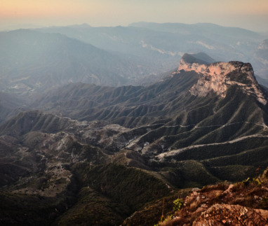 Een weids berglandschap bij zonsopgang gezien vanaf het uitkijkpunt Mirador Cuatro Palos in Mexico, met diepe valleien en een opvallende rotsformatie onder een zachte ochtendlucht.