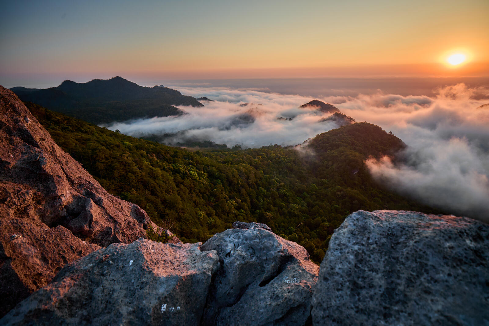 Uitzicht over het berglandschap van de Sierra Gorda bij zonsopgang, gefotografeerd vanuit het dorpje Trinidad in Mexico, met wolken die tussen de beboste heuvels hangen.