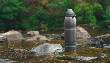 Zwarte Water-to-Go filterfles op een rots in een stromende rivier