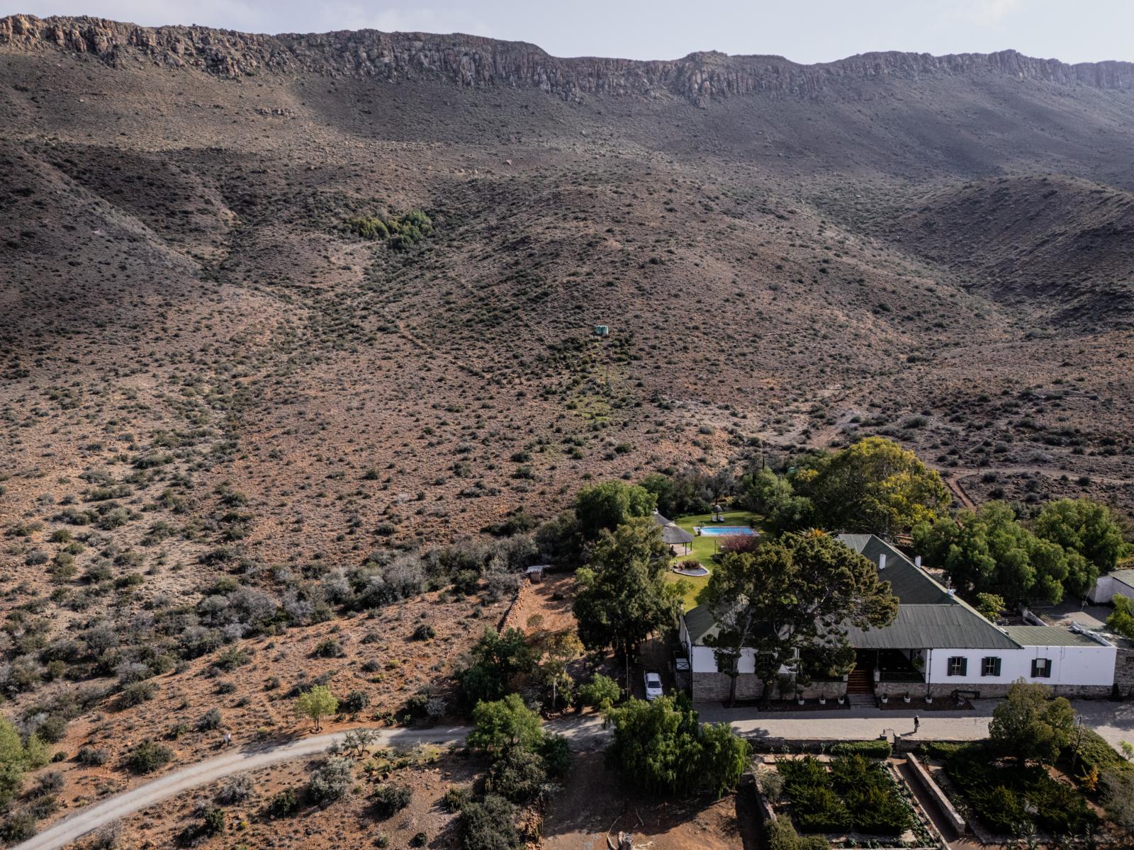 Een bovenaanzicht van de Lemoenfontein Game Lodge, genesteld aan de voet van een uitgestrekte bergketen in het droge landschap van de Zuid-Afrikaanse Karoo.