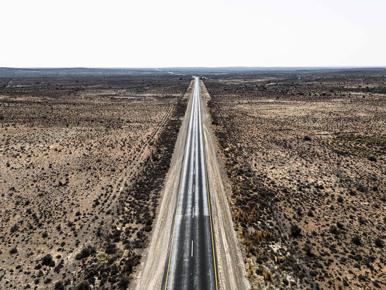 Een bovenaanzicht van een eindeloze, rechte weg die door het dorre en uitgestrekte landschap van de Karoo in Zuid-Afrika snijdt.