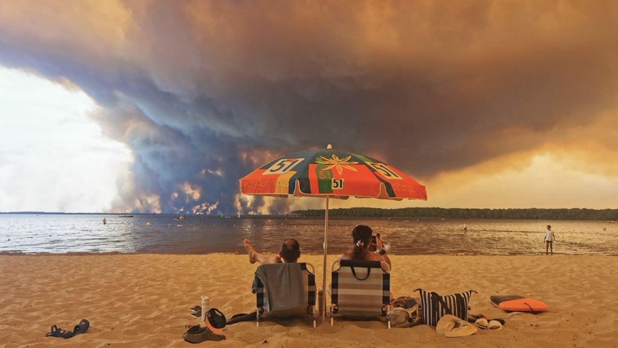 Op 24 juli 2026 rusten strandgangers uit op het strand van Moutchic aan de oever van het Lacanau-meer (Étang de Lacanau) in Lacanau, in het zuidwesten van Frankrijk, terwijl rookwolken opstijgen uit de bosbrand in de Gironde. De brand die woedt in het noordelijke deel van het bekken van Arcachon in de Gironde, in het zuidwesten van Frankrijk, heeft volgens de laatste cijfers van de prefectuur al meer dan 3.400 hectare verwoest. Meer dan 20.000 inwoners en toeristen zijn geëvacueerd uit dit gebied, dat in 2022 al door vlammen was verwoest. Wetenschappers waarschuwen al lang dat de klimaatverandering, veroorzaakt door het gebruik van fossiele brandstoffen door de mens, droogteperiodes intenser en langduriger zal maken, waardoor de ideale omstandigheden voor bosbranden ontstaan.