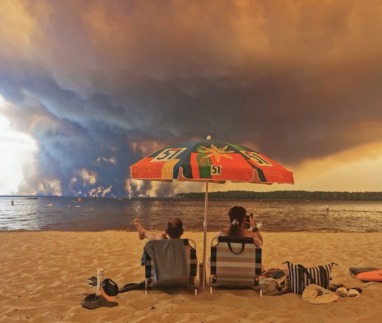 Op 24 juli 2026 rusten strandgangers uit op het strand van Moutchic aan de oever van het Lacanau-meer (Étang de Lacanau) in Lacanau, in het zuidwesten van Frankrijk, terwijl rookwolken opstijgen uit de bosbrand in de Gironde. De brand die woedt in het noordelijke deel van het bekken van Arcachon in de Gironde, in het zuidwesten van Frankrijk, heeft volgens de laatste cijfers van de prefectuur al meer dan 3.400 hectare verwoest. Meer dan 20.000 inwoners en toeristen zijn geëvacueerd uit dit gebied, dat in 2022 al door vlammen was verwoest. Wetenschappers waarschuwen al lang dat de klimaatverandering, veroorzaakt door het gebruik van fossiele brandstoffen door de mens, droogteperiodes intenser en langduriger zal maken, waardoor de ideale omstandigheden voor bosbranden ontstaan.