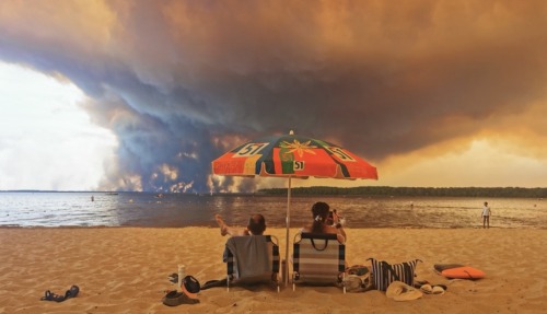 Op 24 juli 2026 rusten strandgangers uit op het strand van Moutchic aan de oever van het Lacanau-meer (Étang de Lacanau) in Lacanau, in het zuidwesten van Frankrijk, terwijl rookwolken opstijgen uit de bosbrand in de Gironde. De brand die woedt in het noordelijke deel van het bekken van Arcachon in de Gironde, in het zuidwesten van Frankrijk, heeft volgens de laatste cijfers van de prefectuur al meer dan 3.400 hectare verwoest. Meer dan 20.000 inwoners en toeristen zijn geëvacueerd uit dit gebied, dat in 2022 al door vlammen was verwoest. Wetenschappers waarschuwen al lang dat de klimaatverandering, veroorzaakt door het gebruik van fossiele brandstoffen door de mens, droogteperiodes intenser en langduriger zal maken, waardoor de ideale omstandigheden voor bosbranden ontstaan.