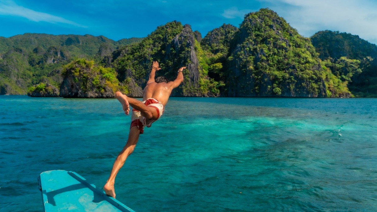 Een jonge man die vanaf een boot in het turquoise water van het eiland Coron in de Filippijnen duikt en geniet van een tropische vakantie