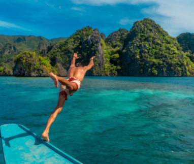 Een jonge man die vanaf een boot in het turquoise water van het eiland Coron in de Filippijnen duikt en geniet van een tropische vakantie