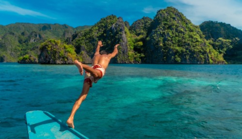 Een jonge man die vanaf een boot in het turquoise water van het eiland Coron in de Filippijnen duikt en geniet van een tropische vakantie
