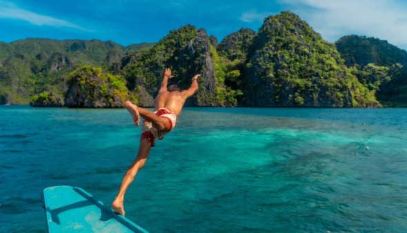 Een jonge man die vanaf een boot in het turquoise water van het eiland Coron in de Filippijnen duikt en geniet van een tropische vakantie