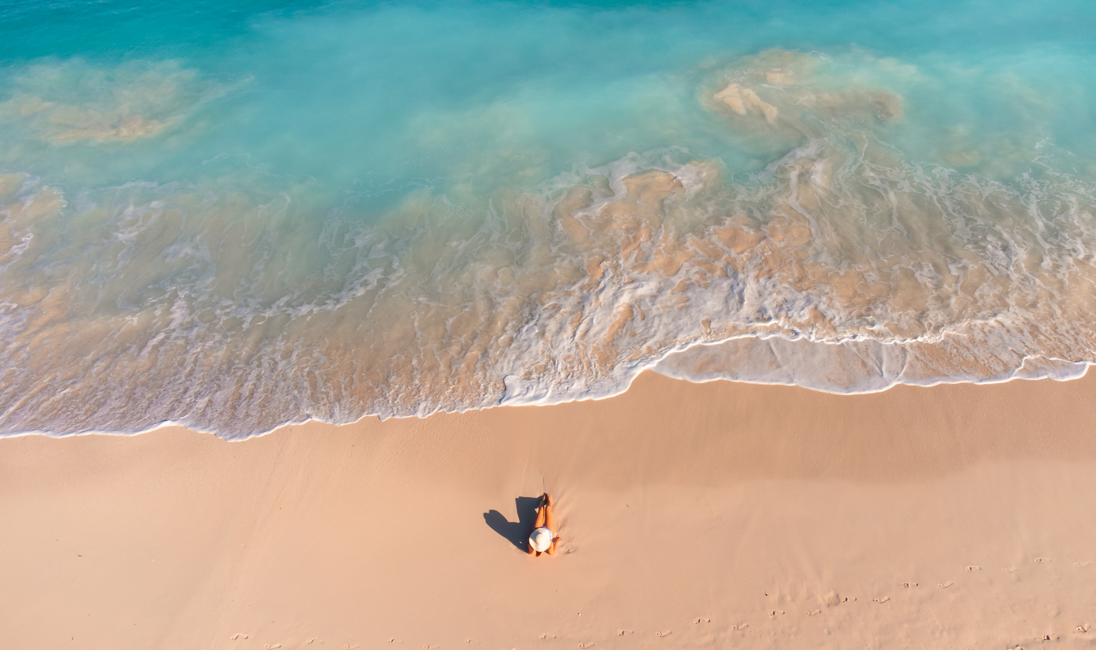 Luchtfoto van een vrouw op een zandstrand terwijl de golven van de oceaan aanrollen