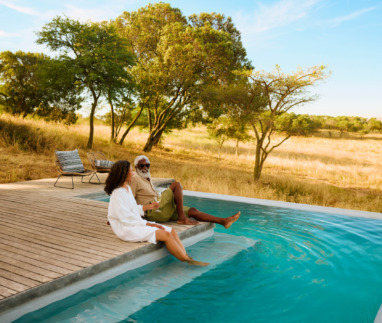 Een volwassen stel geniet van een luxe safarivakantie en laat hun voeten in een zwembad met uitzicht op de savanne hangen