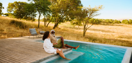 Een volwassen stel geniet van een luxe safarivakantie en laat hun voeten in een zwembad met uitzicht op de savanne hangen