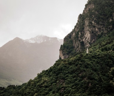 Kleine Mariakapel op een beboste berghelling in Valchiavenna, omringd door steile rotswanden en Alpentoppen