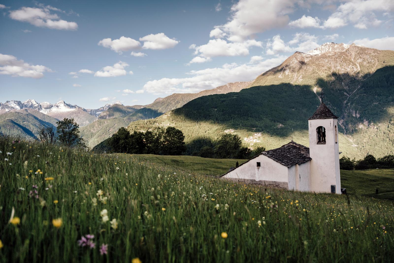 Kleine bergkapel in een bloemenweide met uitzicht op de bergen van Valchiavenna in Noord-Italië