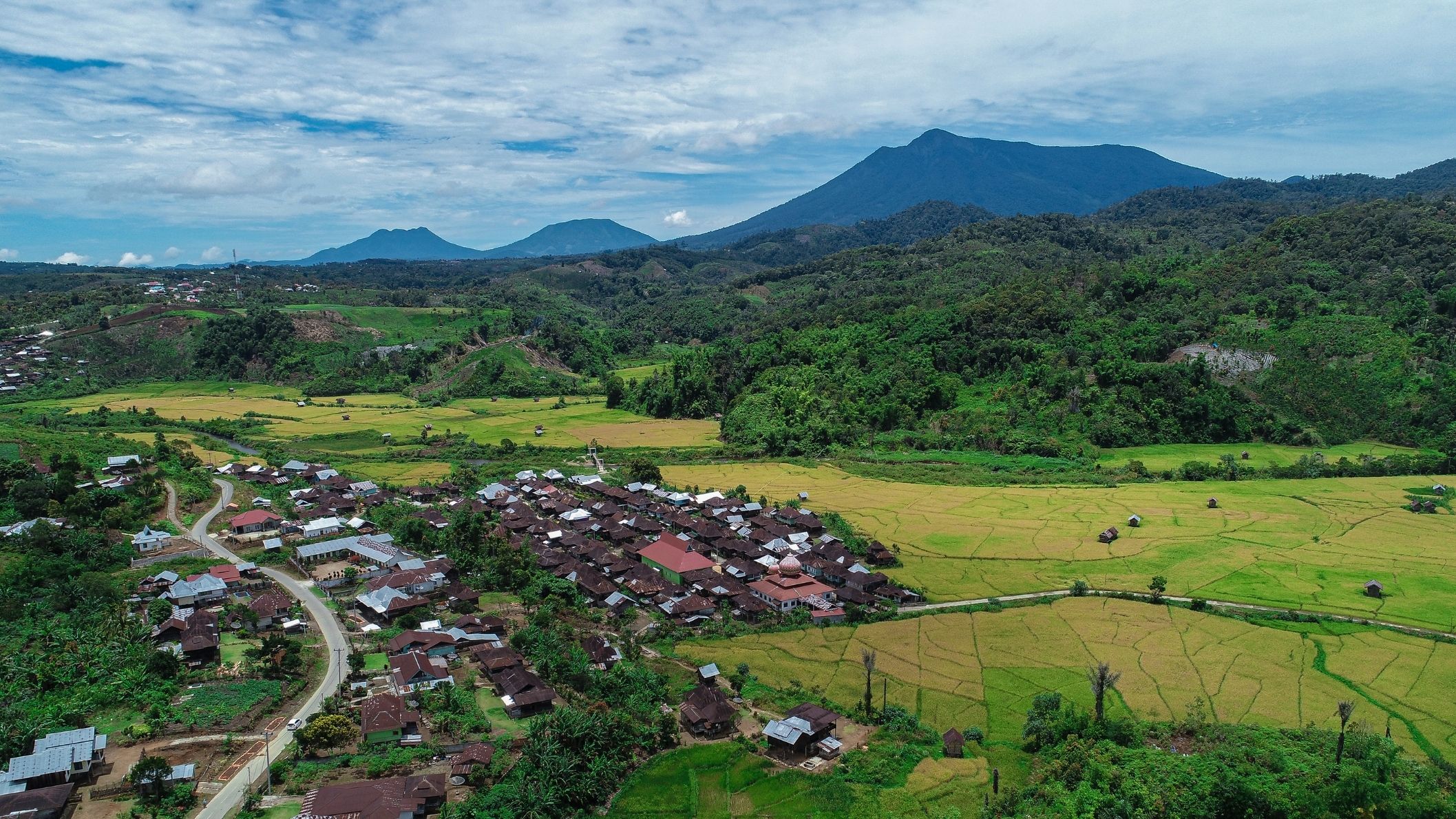 Luchtfoto van het dorp Bangko omringd door groene rijstvelden, bossen en bergen op Sumatra.