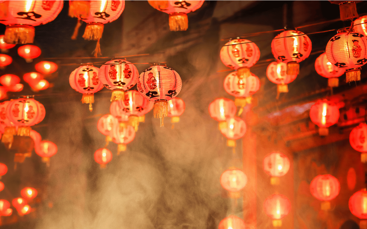 Een groot aantal helder verlichte rode Chinese lantaarns hangt in clusters, verlicht door kaarslicht en omgeven door sfeervolle rook en nevel, tijdens een festival in Thailand.