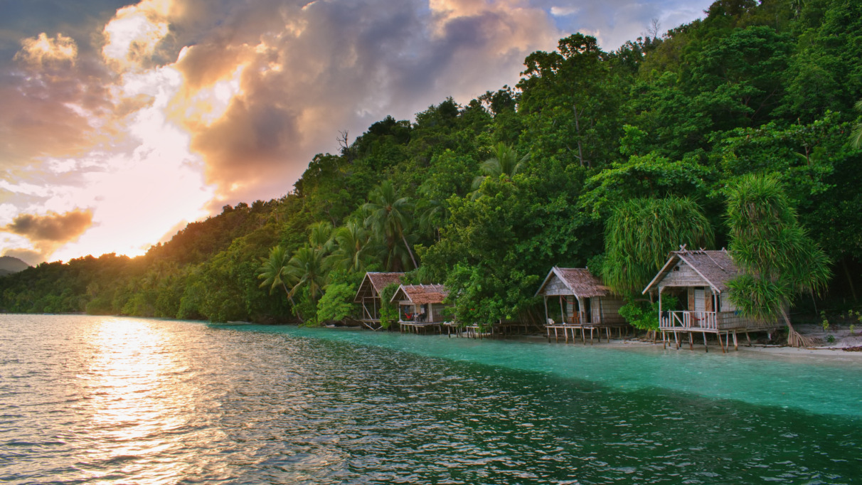 Prachtige zonsondergang boven typische houten bungalows aan het strand – het eiland Kri, Raja Ampat, West-Papoea, Indonesië