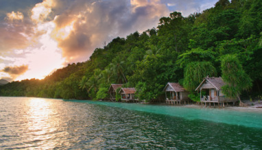 Prachtige zonsondergang boven typische houten bungalows aan het strand – het eiland Kri, Raja Ampat, West-Papoea, Indonesië