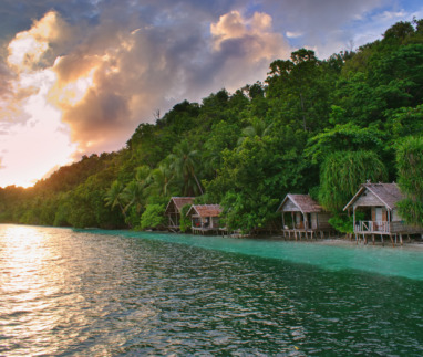 Prachtige zonsondergang boven typische houten bungalows aan het strand – het eiland Kri, Raja Ampat, West-Papoea, Indonesië