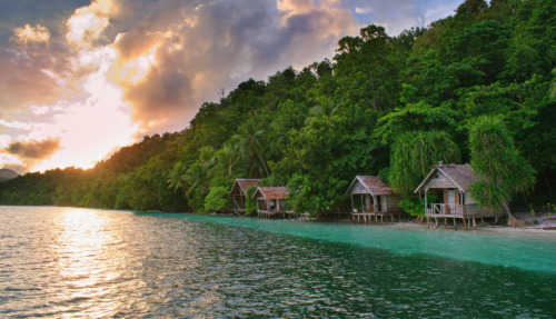 Prachtige zonsondergang boven typische houten bungalows aan het strand – het eiland Kri, Raja Ampat, West-Papoea, Indonesië