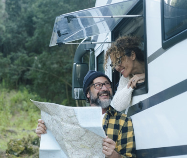 Een gelukkig, volwassen stel geniet van het camperleven: ze reizen, praten en bekijken samen een kaart om hun volgende vakantiebestemming te kiezen. De man staat buiten en de vrouw zit bij het raam. Camper