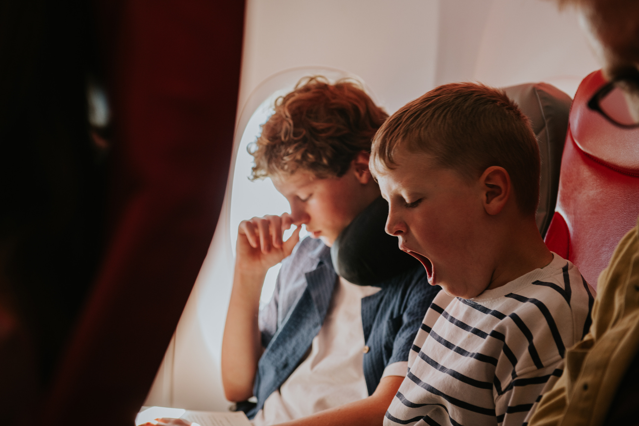 Twee jonge jongens wachten geduldig op hun vlucht naar hun vakantiebestemming. Het jongere broertje gaapt.