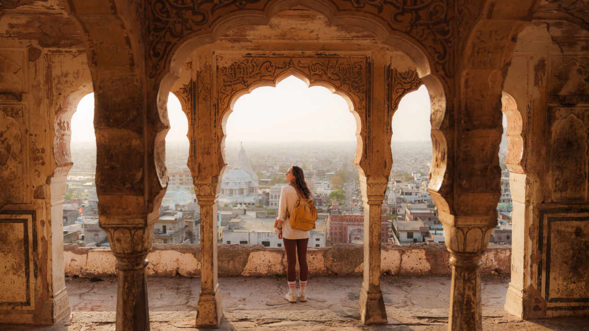 Vrouw die vanuit een oud gebouw in Mughal-stijl naar het stadsgezicht van Jaipur bij zonsondergang kijkt