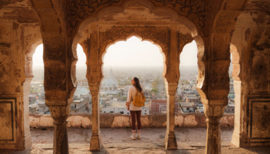 Vrouw die vanuit een oud gebouw in Mughal-stijl naar het stadsgezicht van Jaipur bij zonsondergang kijkt