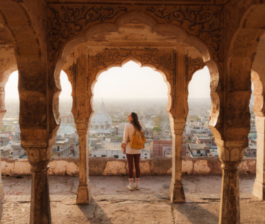 Vrouw die vanuit een oud gebouw in Mughal-stijl naar het stadsgezicht van Jaipur bij zonsondergang kijkt