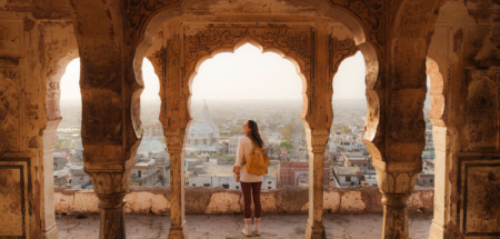 Vrouw die vanuit een oud gebouw in Mughal-stijl naar het stadsgezicht van Jaipur bij zonsondergang kijkt