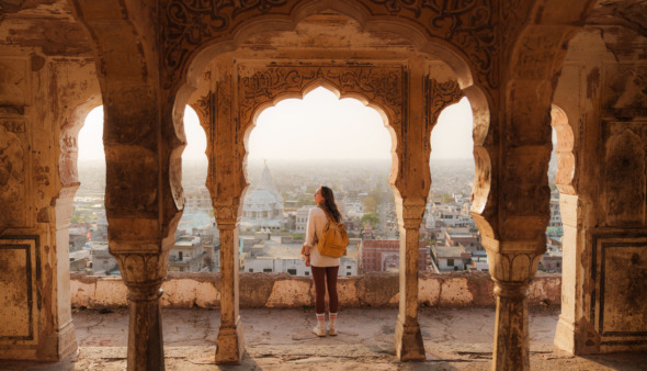 Vrouw die vanuit een oud gebouw in Mughal-stijl naar het stadsgezicht van Jaipur bij zonsondergang kijkt