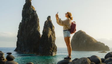 Vrolijke vrouw die met haar smartphone foto’s maakt en geniet van een adembenemend uitzicht op de kust met rotsformaties op het eiland Madeira