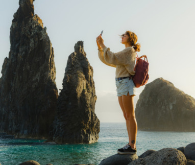 Vrolijke vrouw die met haar smartphone foto’s maakt en geniet van een adembenemend uitzicht op de kust met rotsformaties op het eiland Madeira