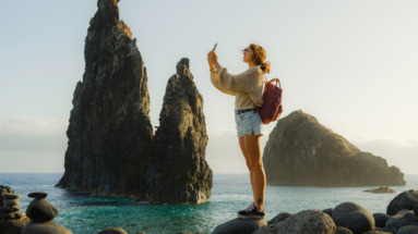 Vrolijke vrouw die met haar smartphone foto’s maakt en geniet van een adembenemend uitzicht op de kust met rotsformaties op het eiland Madeira