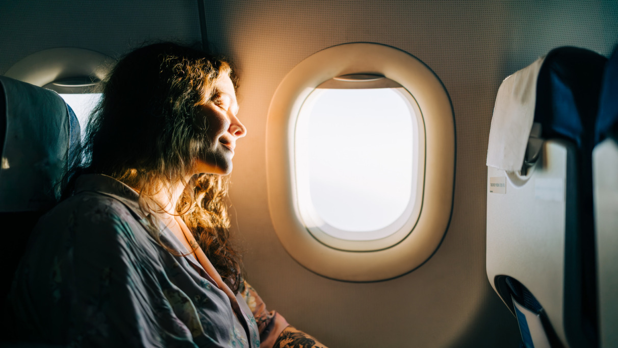 Een ontspannen vrouwelijke passagier geniet van het zonnige uitzicht vanuit het vliegtuigraam