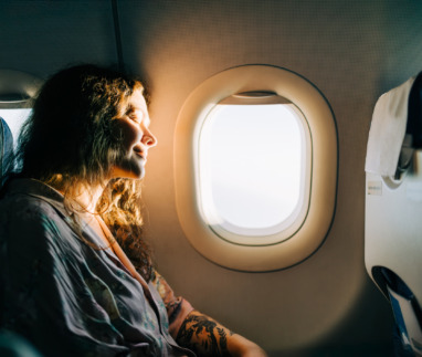 Een ontspannen vrouwelijke passagier geniet van het zonnige uitzicht vanuit het vliegtuigraam