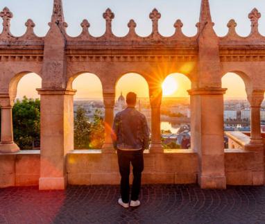 Man die tussen de bogen staat en bij zonsopgang vanaf het Vissersbastion uitkijkt over het stadsgezicht van Boedapest, Hongarije